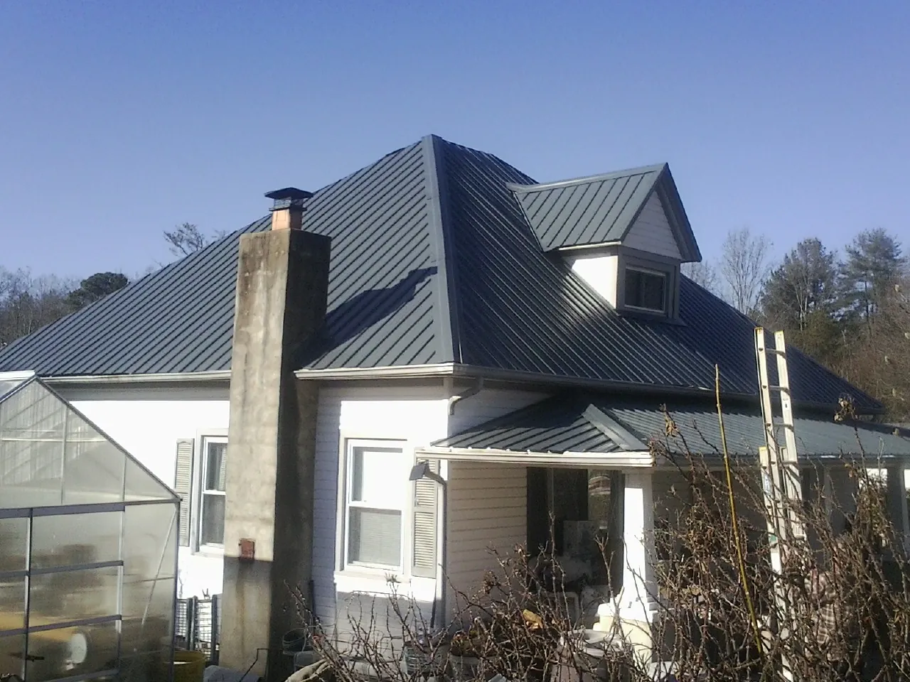 Dark blue standing seam metal roof on a white farmhouse with dormer — Slate & Tile Roof Repair by Roofing Brothers in Medon