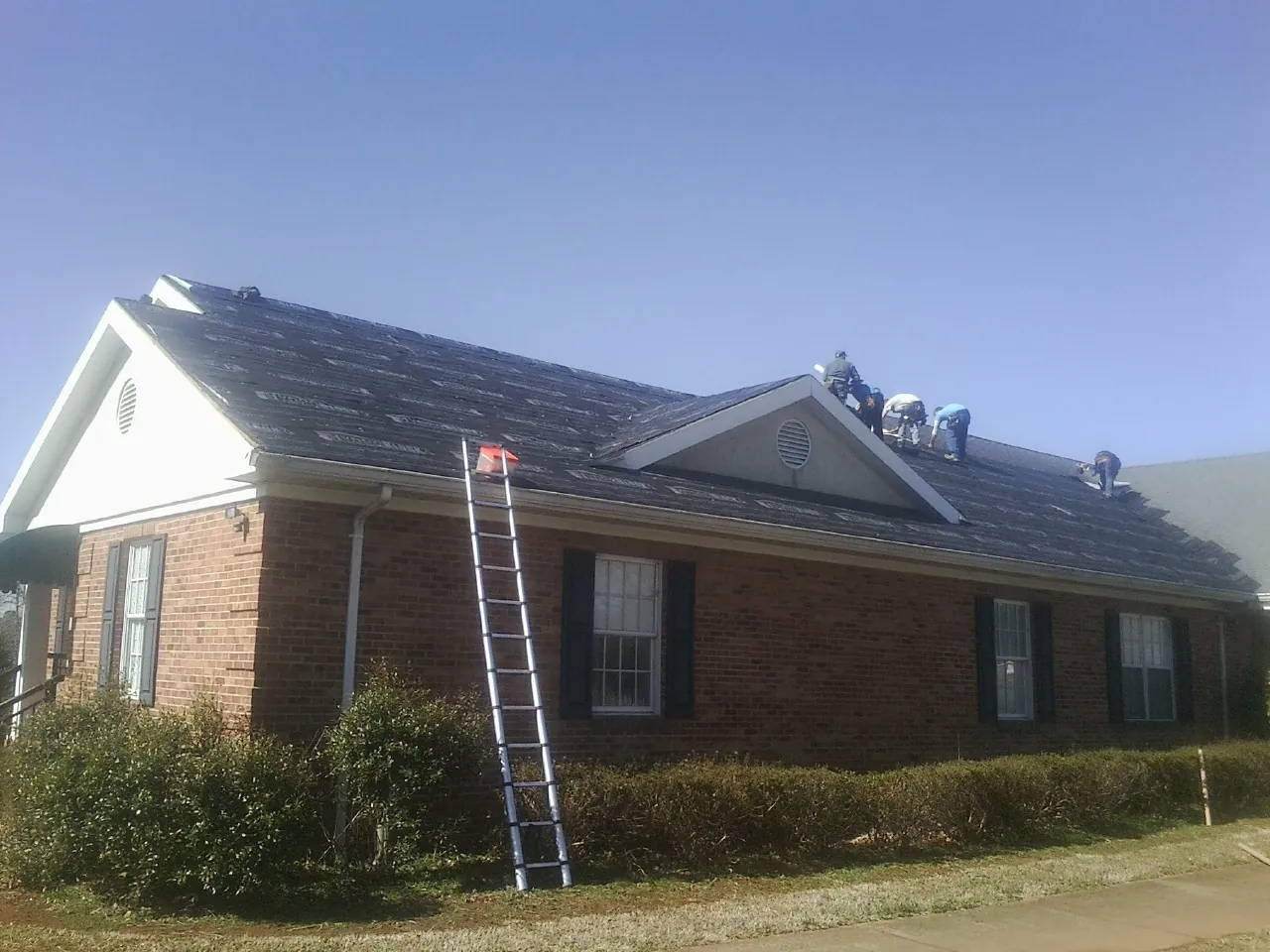Crew tearing shingles off a brick ranch roof with a ladder set — Emergency Roof Repair work by our crew in Medon