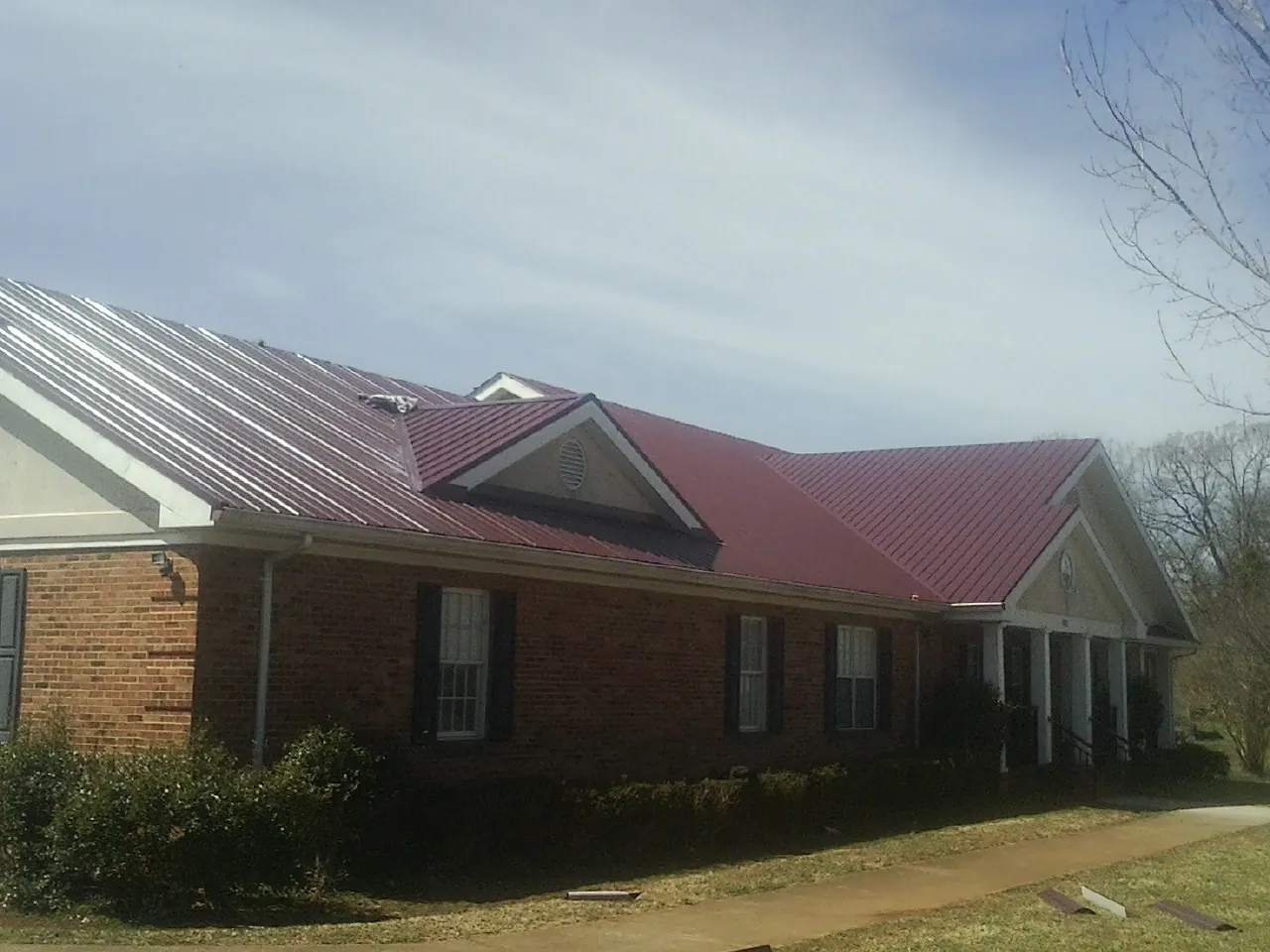 Red metal roof with gabled entries on a long brick building, from a Hail Damage Roof Repair job in Medon