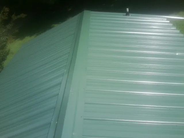 New green metal panels meeting at the ridge of a roof — Flat Roof Repair work by our crew in Medon