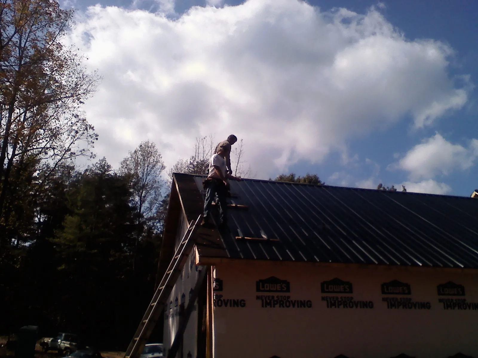 Roofer fastening dark metal panels high against a cloudy sky, from a Roof Inspection job in Medon