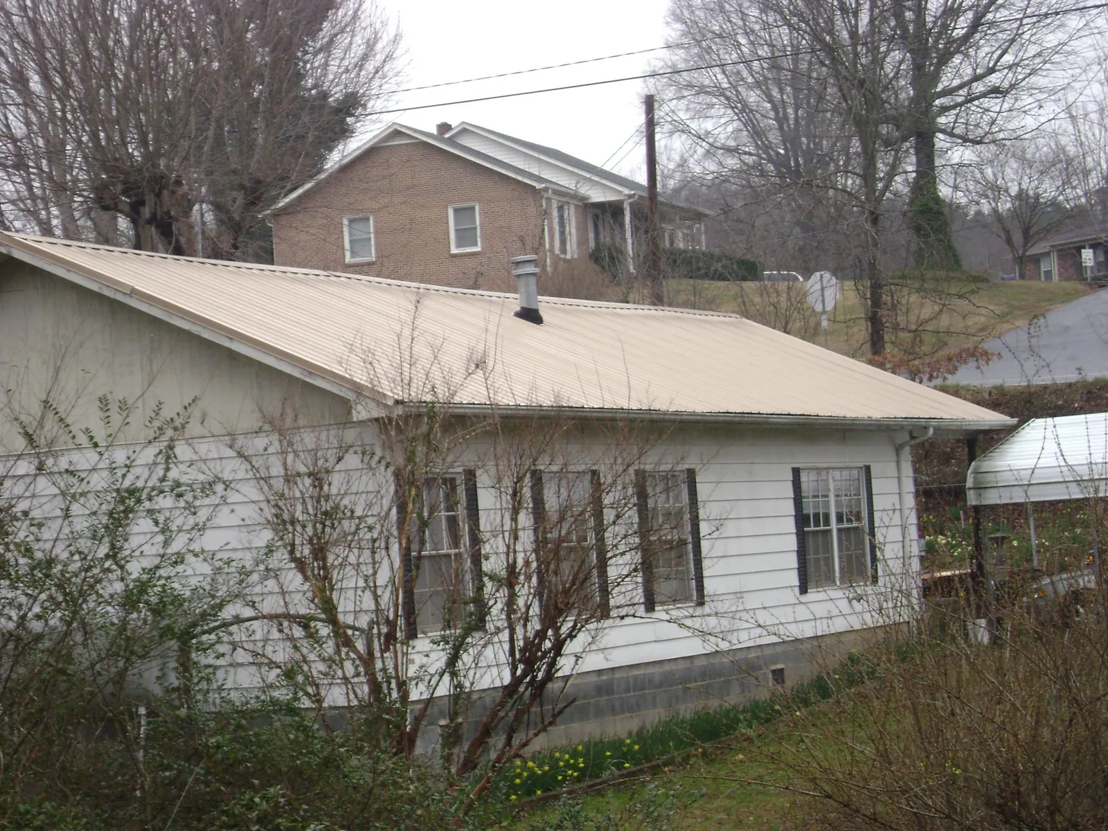 Tan metal roof on a white sided house set into a hillside — Commercial Roofing by Roofing Brothers in Medon